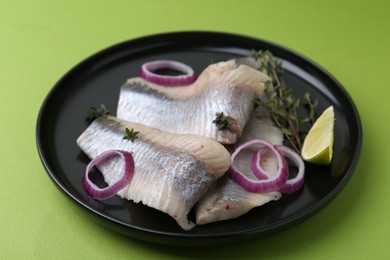 Marinated herring fillets with onion rings, thyme and lime on green background, closeup