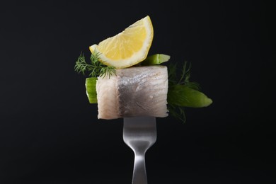 Photo of Fork with marinated herring fillet, cucumber, dill and lemon on black background, closeup