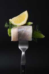 Photo of Fork with marinated herring fillet, cucumber, dill and lemon on black background, closeup