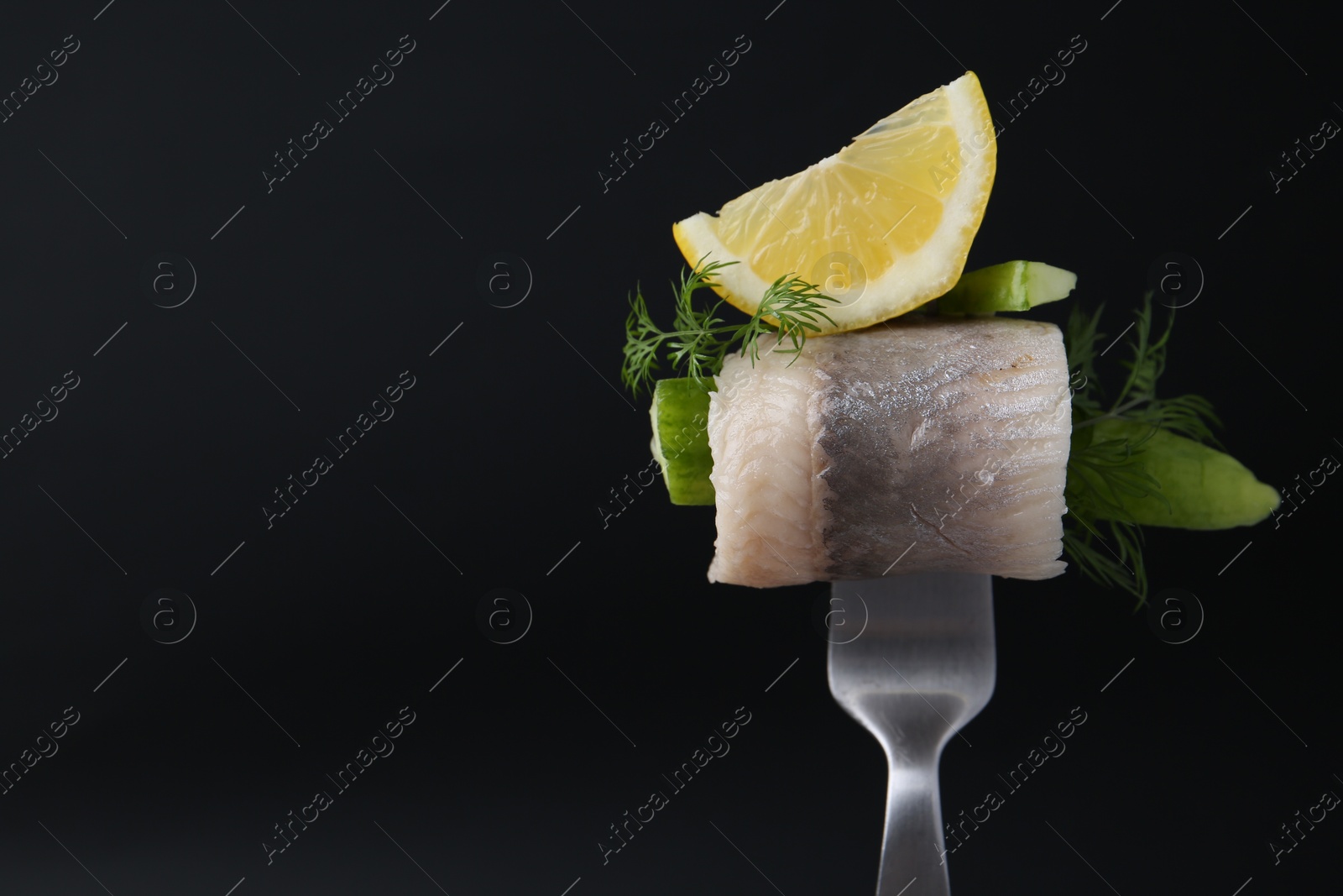 Photo of Fork with marinated herring fillet, cucumber, dill and lemon on black background, closeup. Space for text