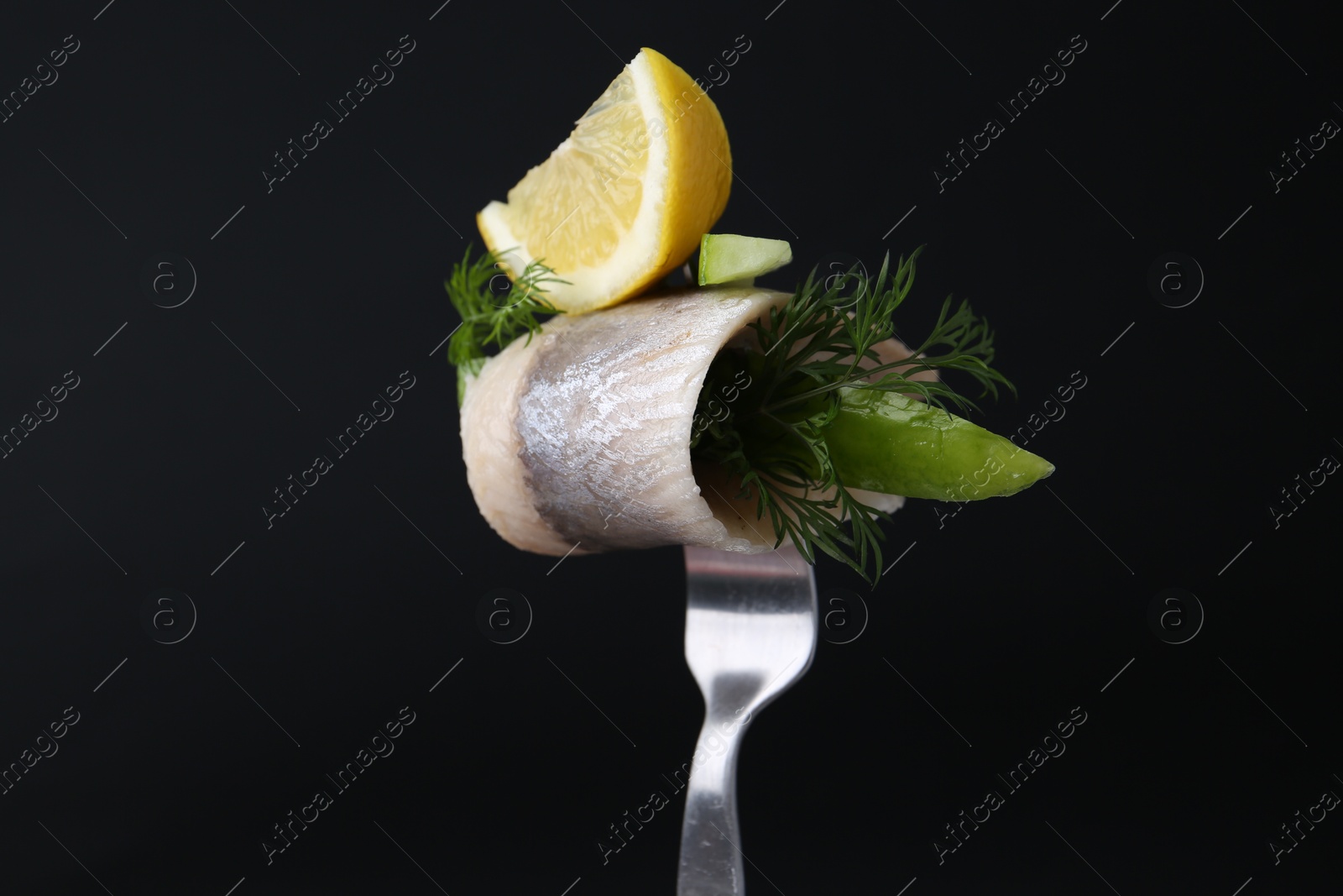 Photo of Fork with marinated herring fillet, cucumber, dill and lemon on black background, closeup