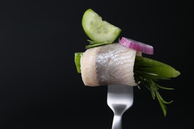 Fork with marinated herring fillet, cucumber, rosemary and onion ring on black background, closeup. Space for text