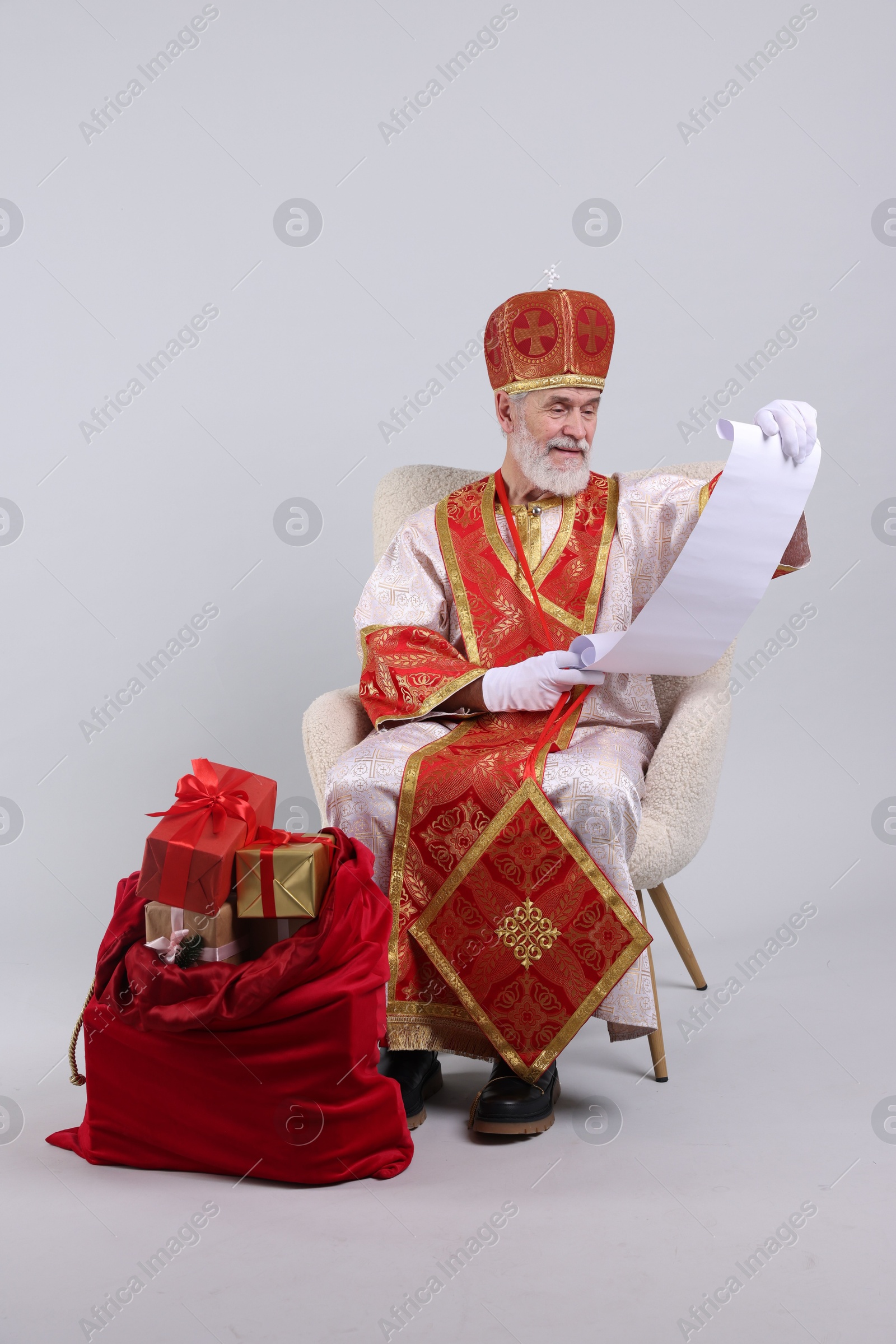 Photo of Saint Nicholas with wish list and sack full of gifts on light grey background