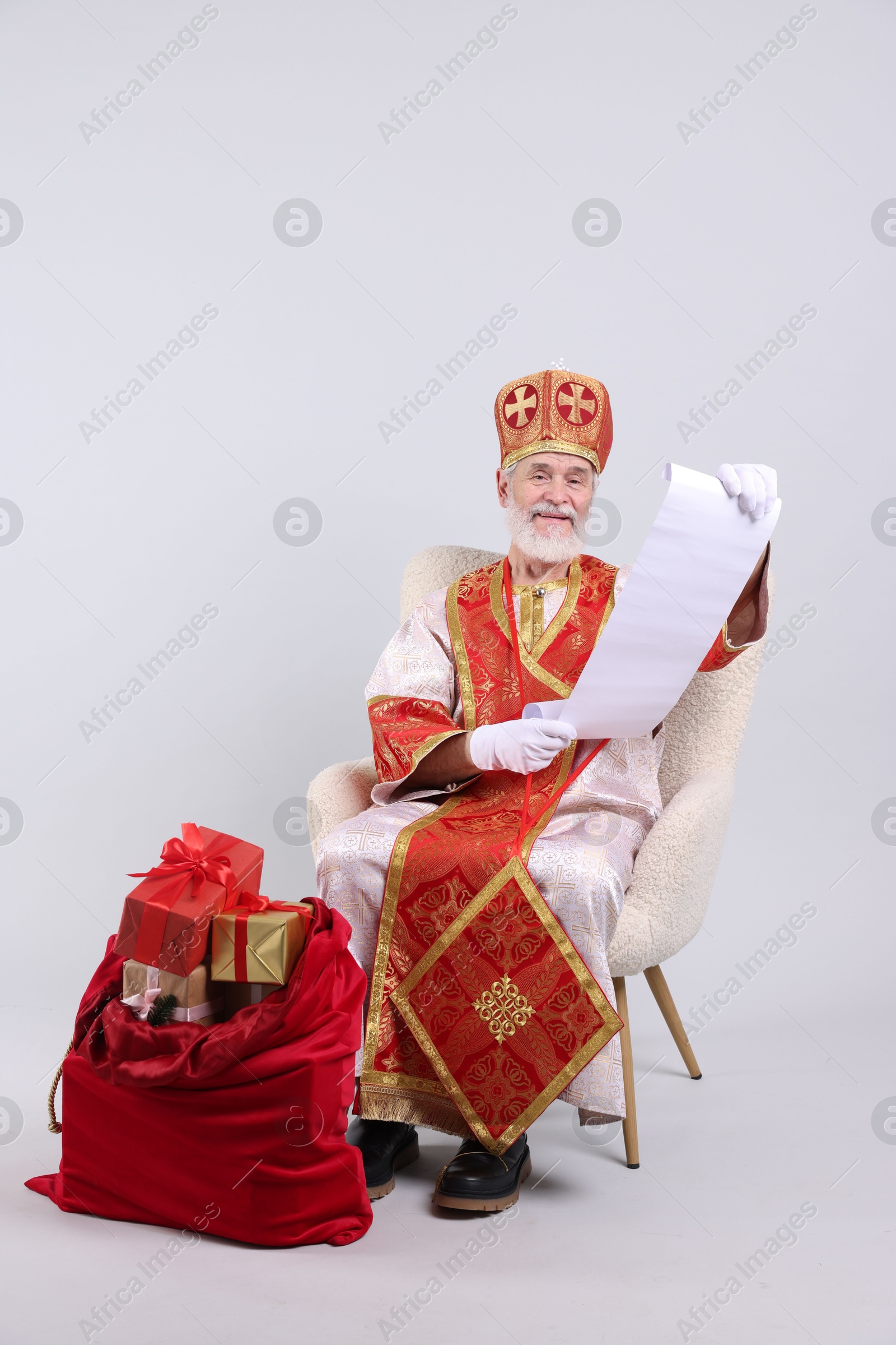 Photo of Saint Nicholas with wish list and sack full of gifts on light grey background