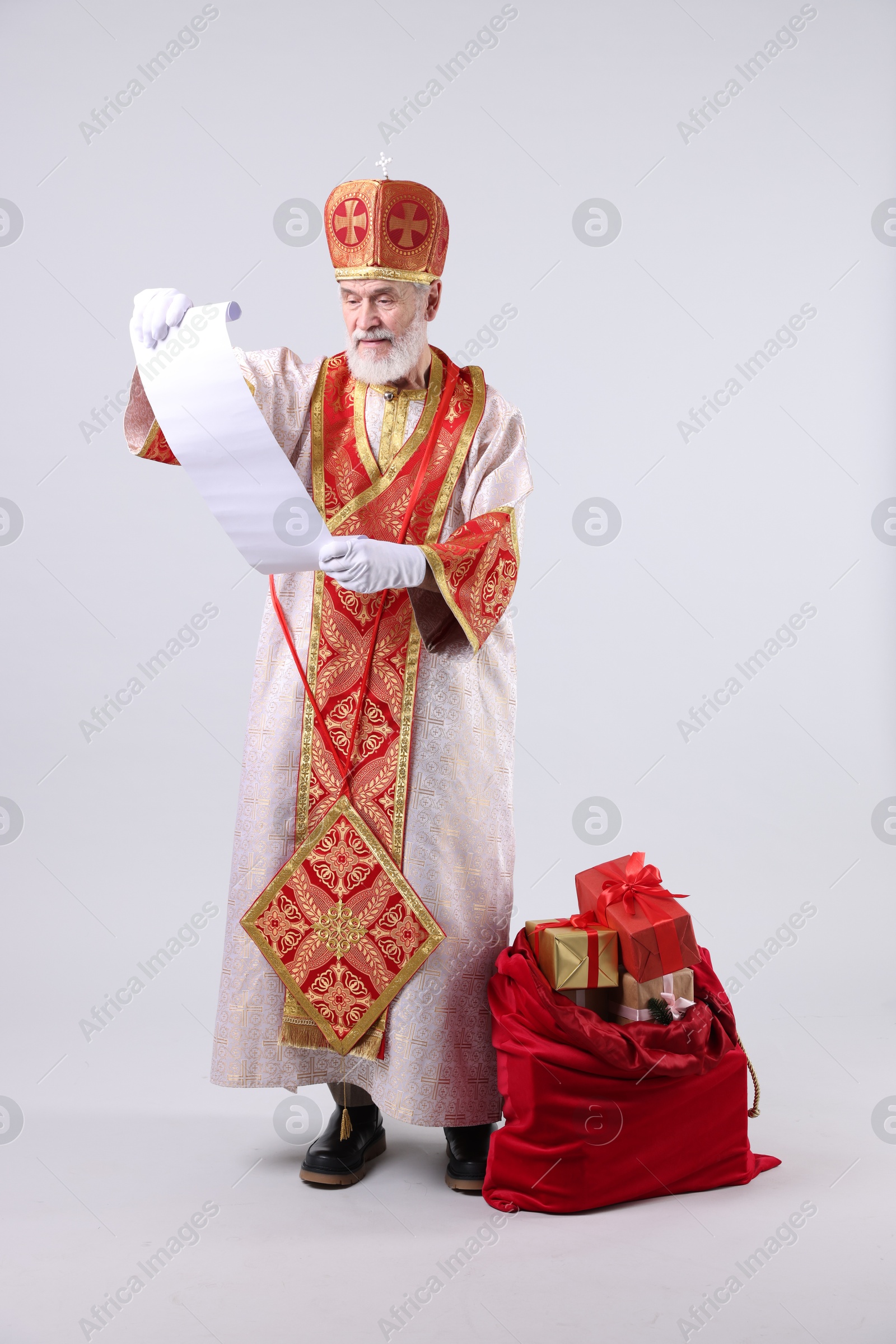 Photo of Saint Nicholas with wish list and sack full of gifts on light grey background