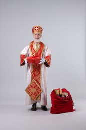 Saint Nicholas with sack full of gifts on light grey background