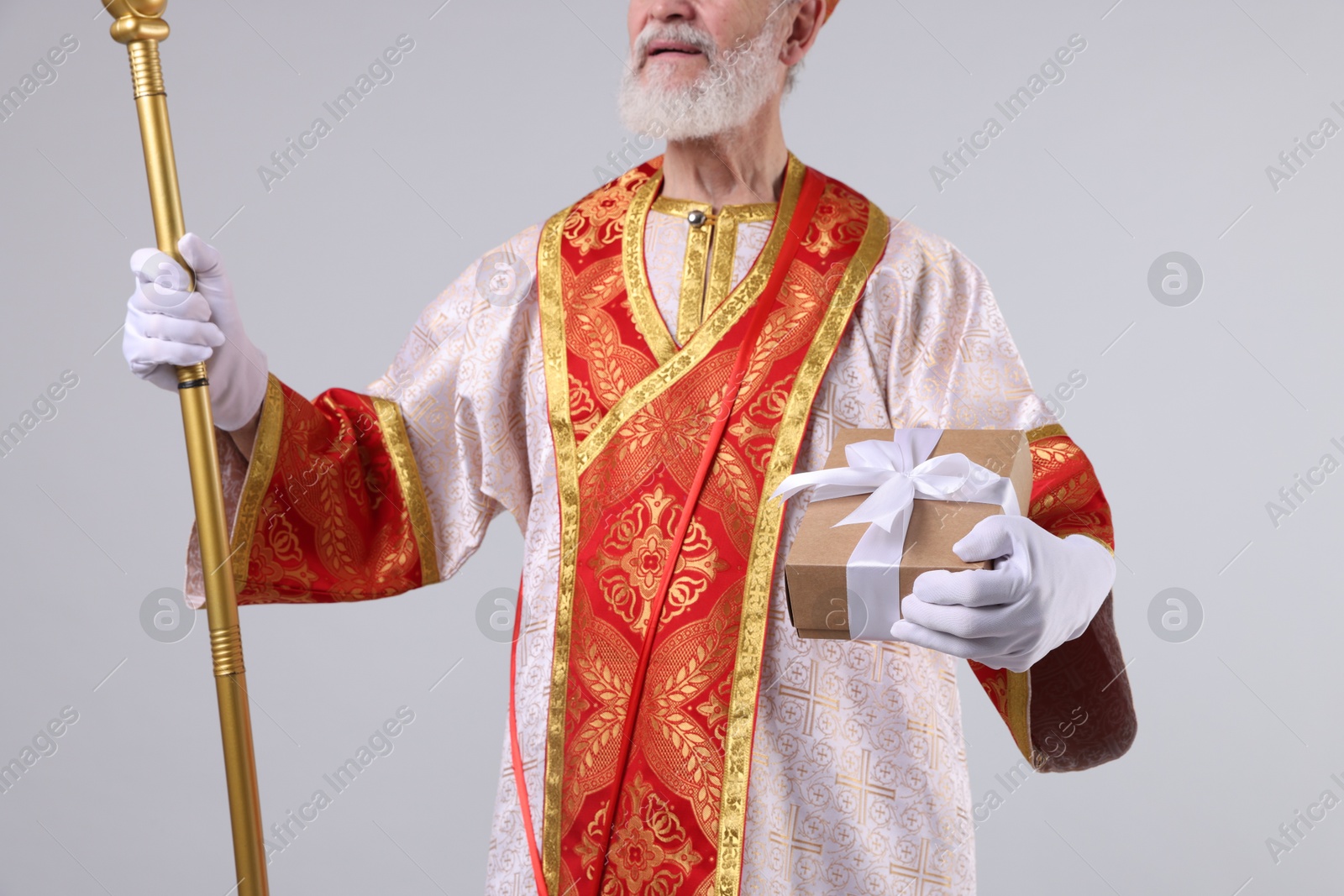 Photo of Saint Nicholas with gift on light grey background, closeup