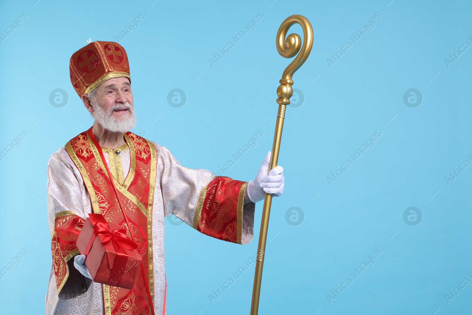 Photo of Saint Nicholas with gift on light blue background. Space for text