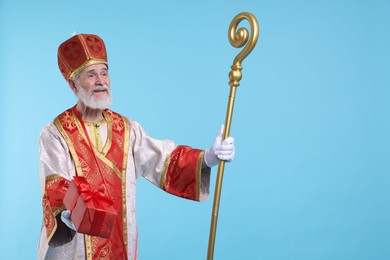 Photo of Saint Nicholas with gift on light blue background. Space for text