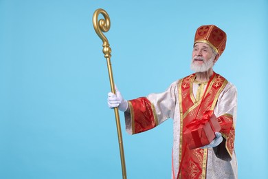 Photo of Saint Nicholas with gift on light blue background. Space for text