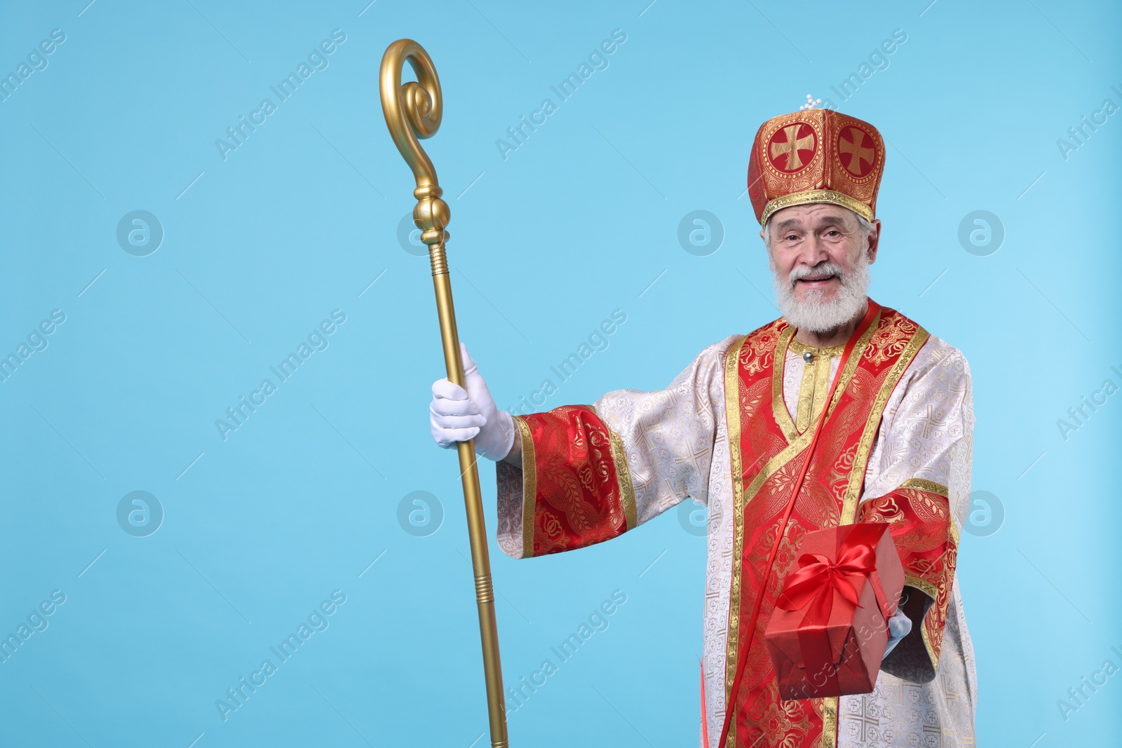 Photo of Saint Nicholas with gift on light blue background. Space for text