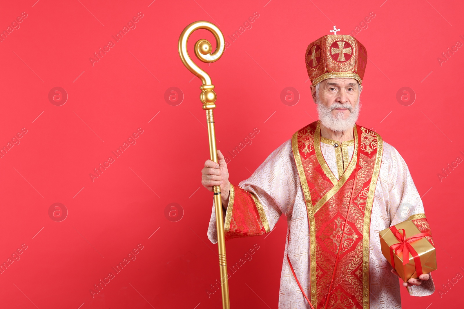 Photo of Saint Nicholas with gift on red background. Space for text