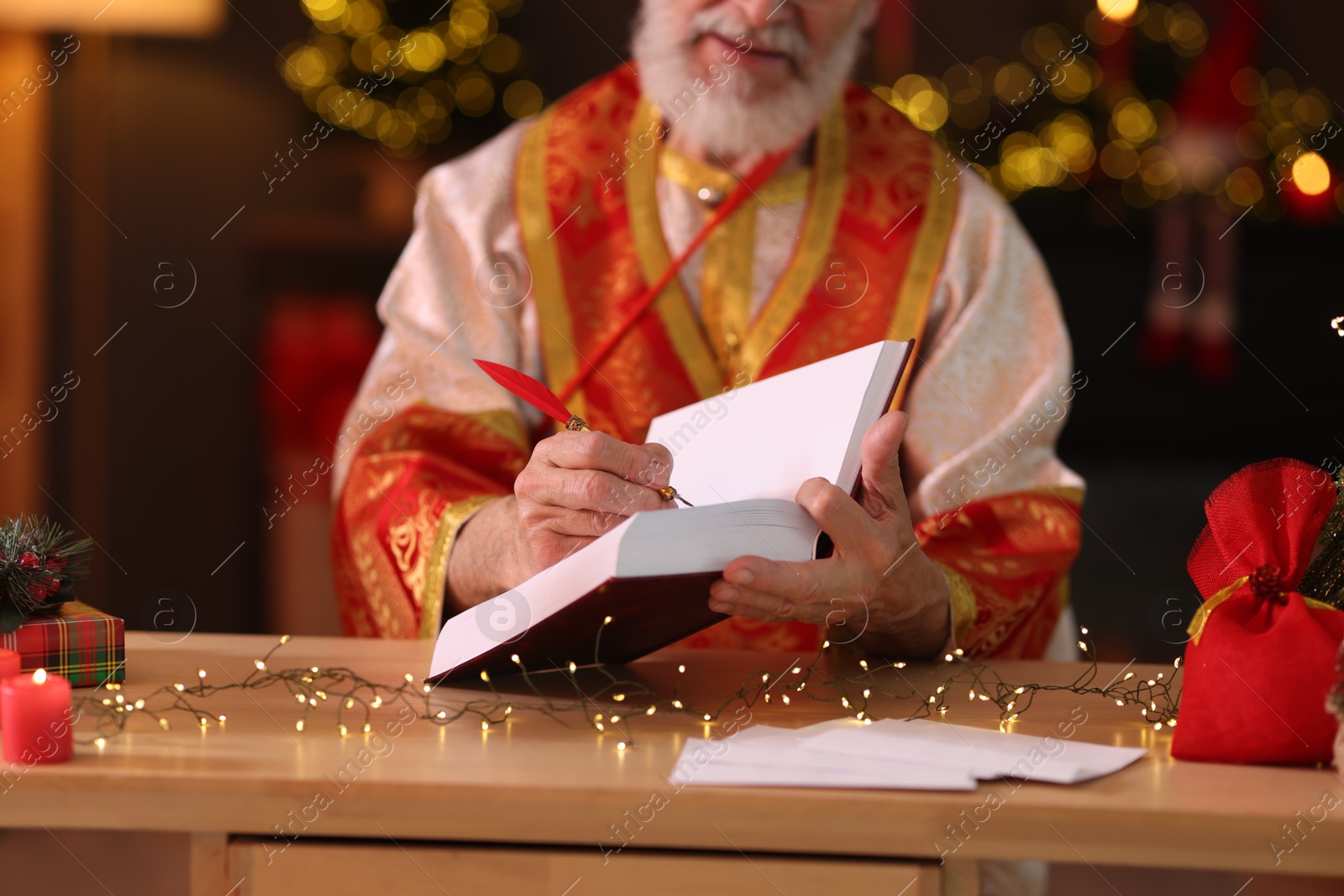 Photo of Saint Nicholas with notebook at desk in room decorated for Christmas, closeup