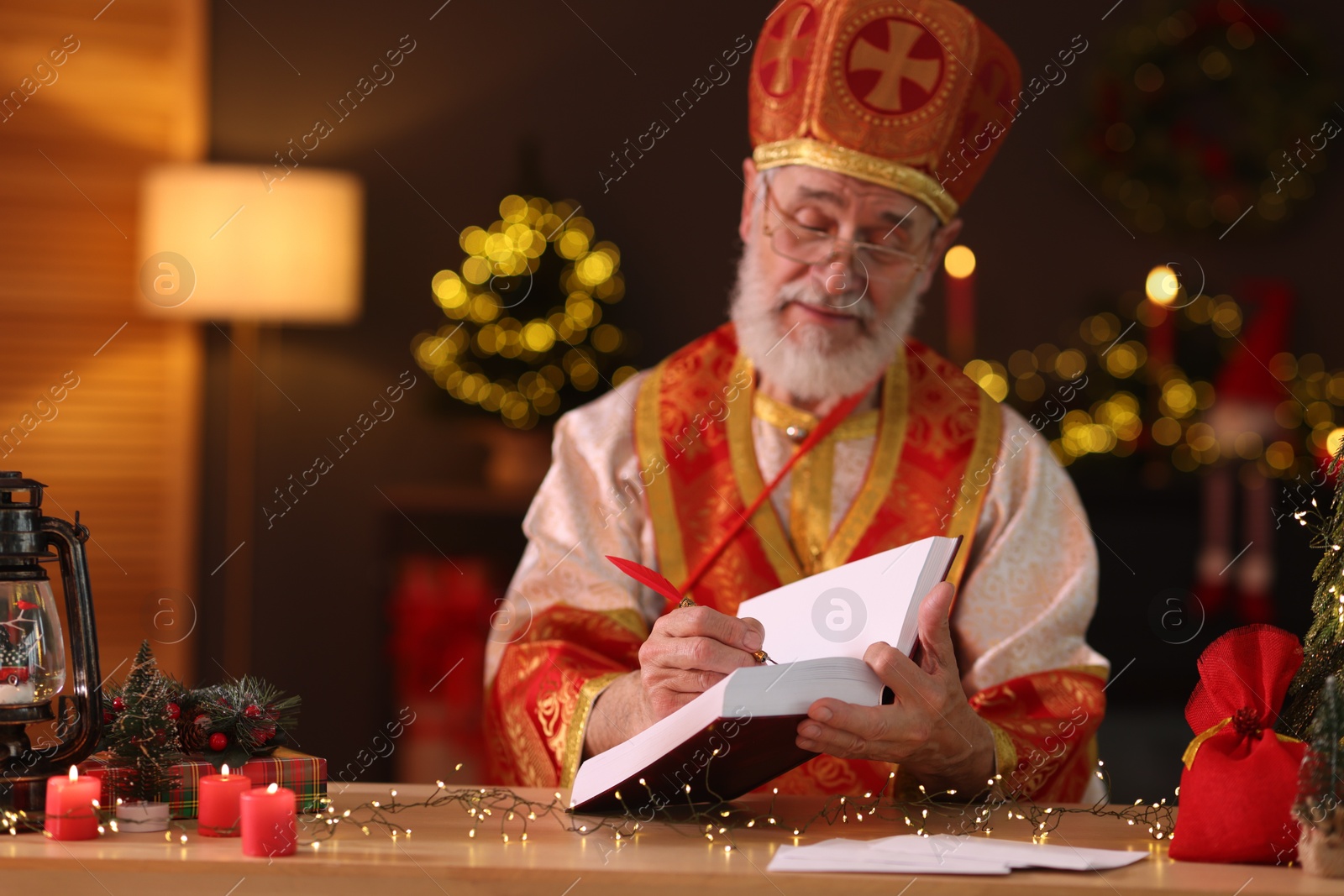 Photo of Saint Nicholas with notebook at desk in room decorated for Christmas