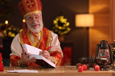 Photo of Saint Nicholas with notebook at desk in room decorated for Christmas