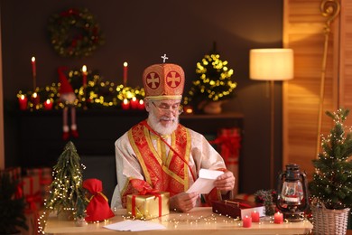 Photo of Saint Nicholas with letter at desk in room decorated for Christmas