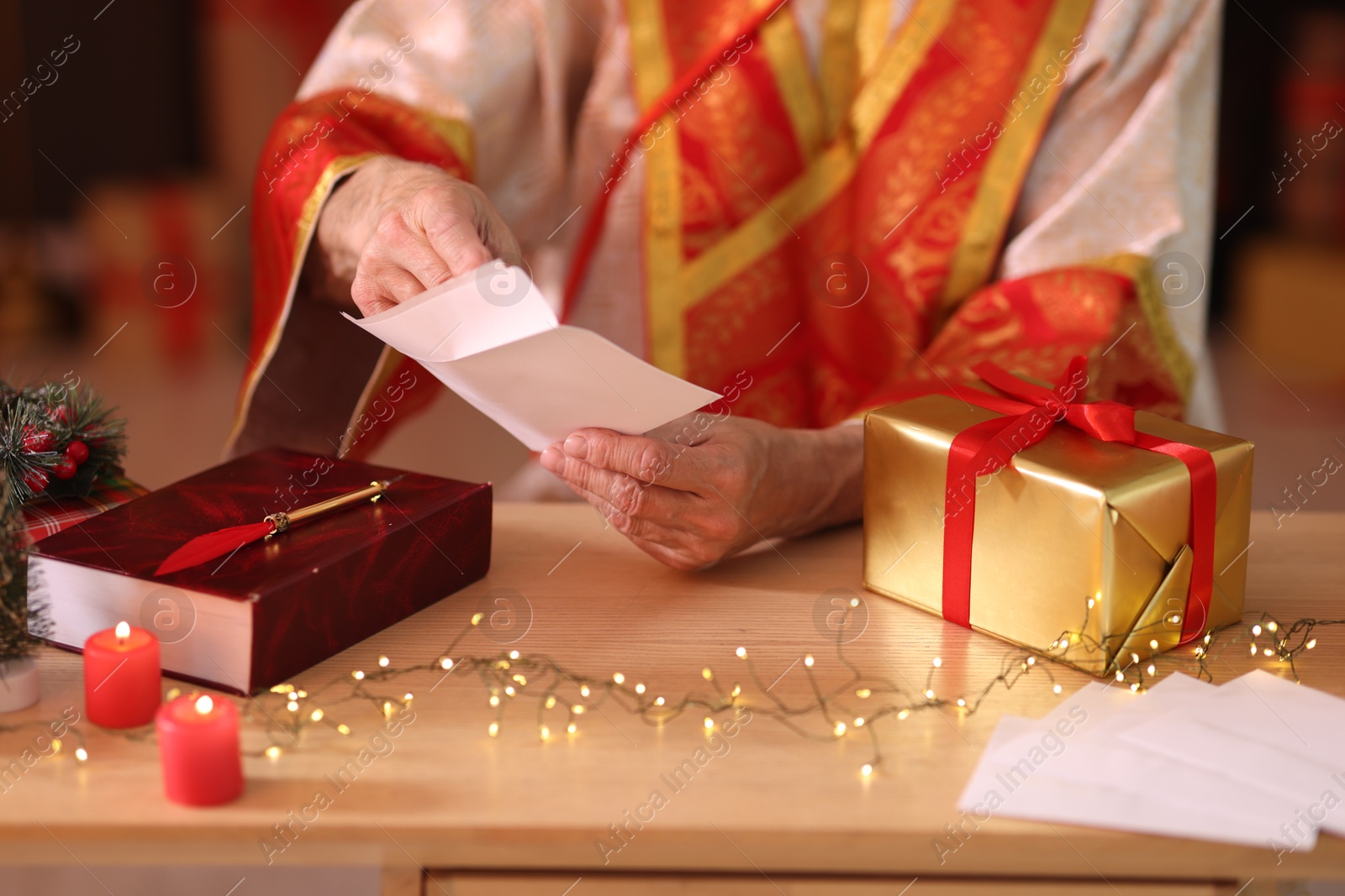 Photo of Saint Nicholas with letter at desk in room decorated for Christmas, closeup