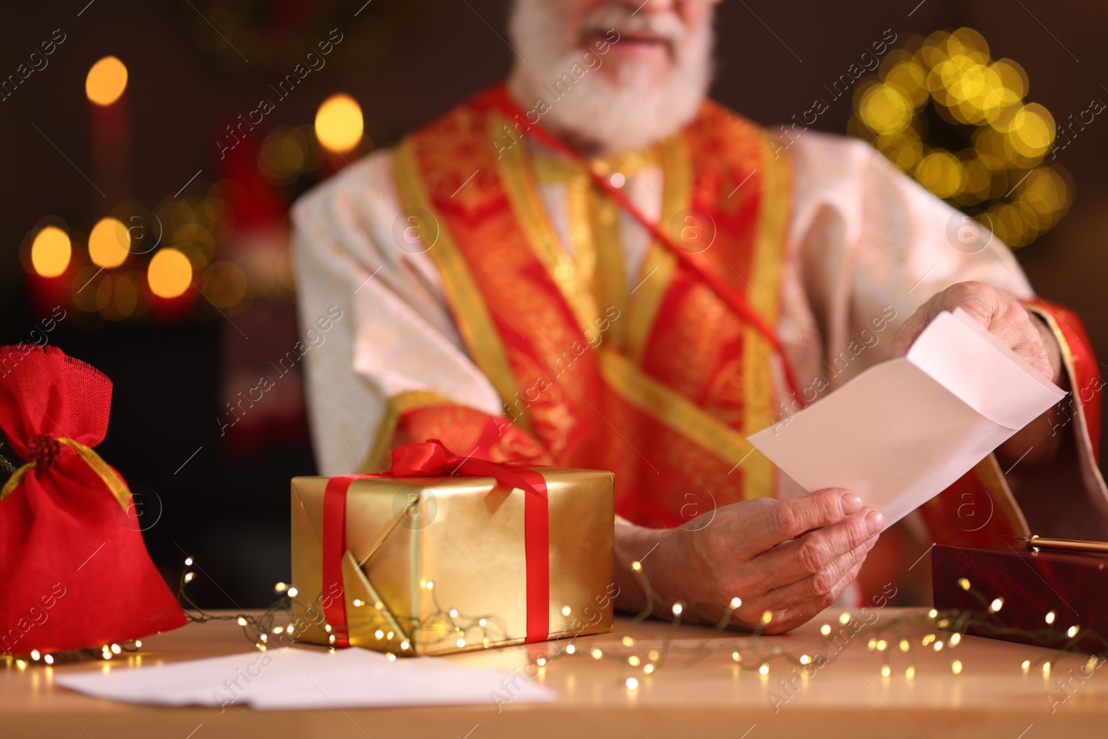 Photo of Saint Nicholas with letter at desk in room decorated for Christmas, closeup