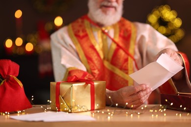 Saint Nicholas with letter at desk in room decorated for Christmas, closeup