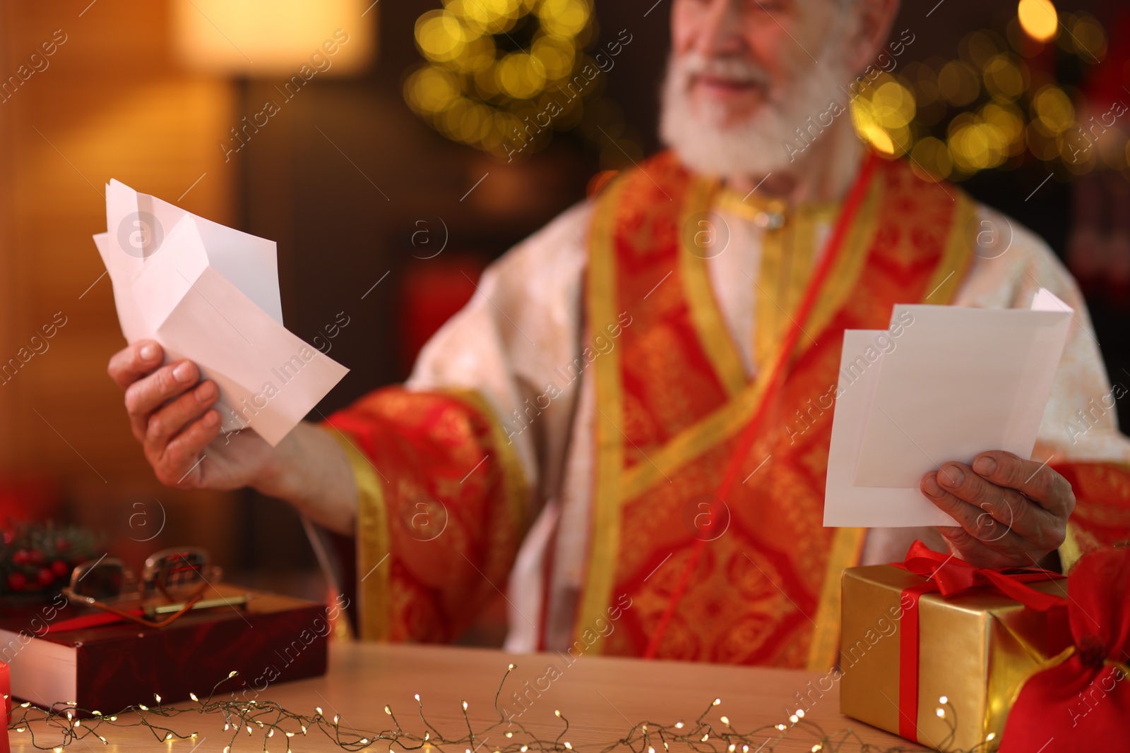 Photo of Saint Nicholas with letters at desk in room decorated for Christmas, closeup