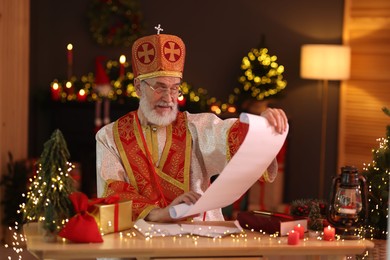 Photo of Saint Nicholas with gift list at desk in room decorated for Christmas