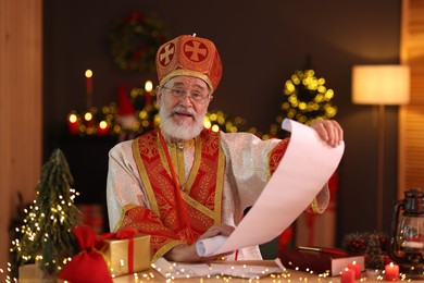 Photo of Saint Nicholas with gift list at desk in room decorated for Christmas