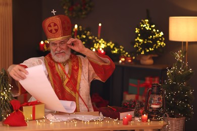 Photo of Saint Nicholas with gift list at desk in room decorated for Christmas