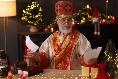 Photo of Saint Nicholas with letters at desk in room decorated for Christmas