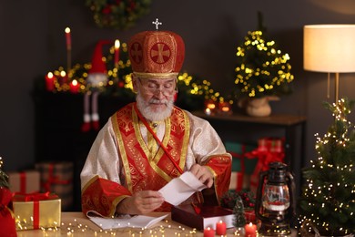 Photo of Saint Nicholas with letters at desk in room decorated for Christmas