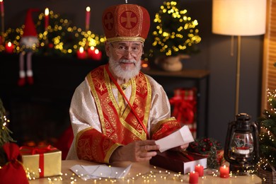 Photo of Saint Nicholas with letters at desk in room decorated for Christmas