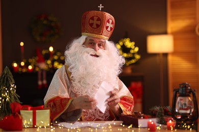 Photo of Saint Nicholas with letters at desk in room decorated for Christmas