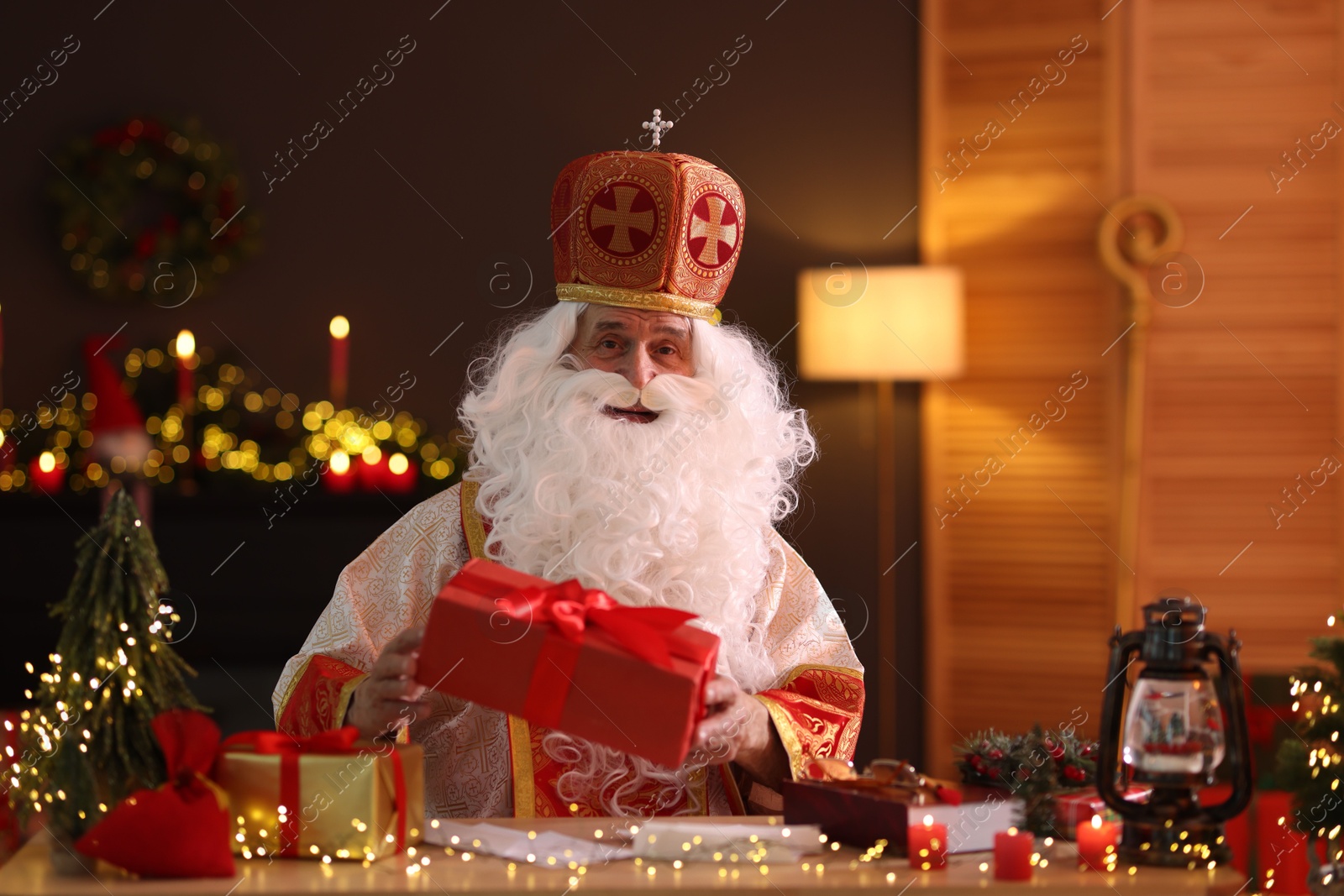 Photo of Saint Nicholas with gifts at desk in room decorated for Christmas