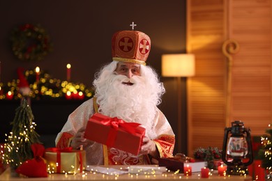 Photo of Saint Nicholas with gifts at desk in room decorated for Christmas