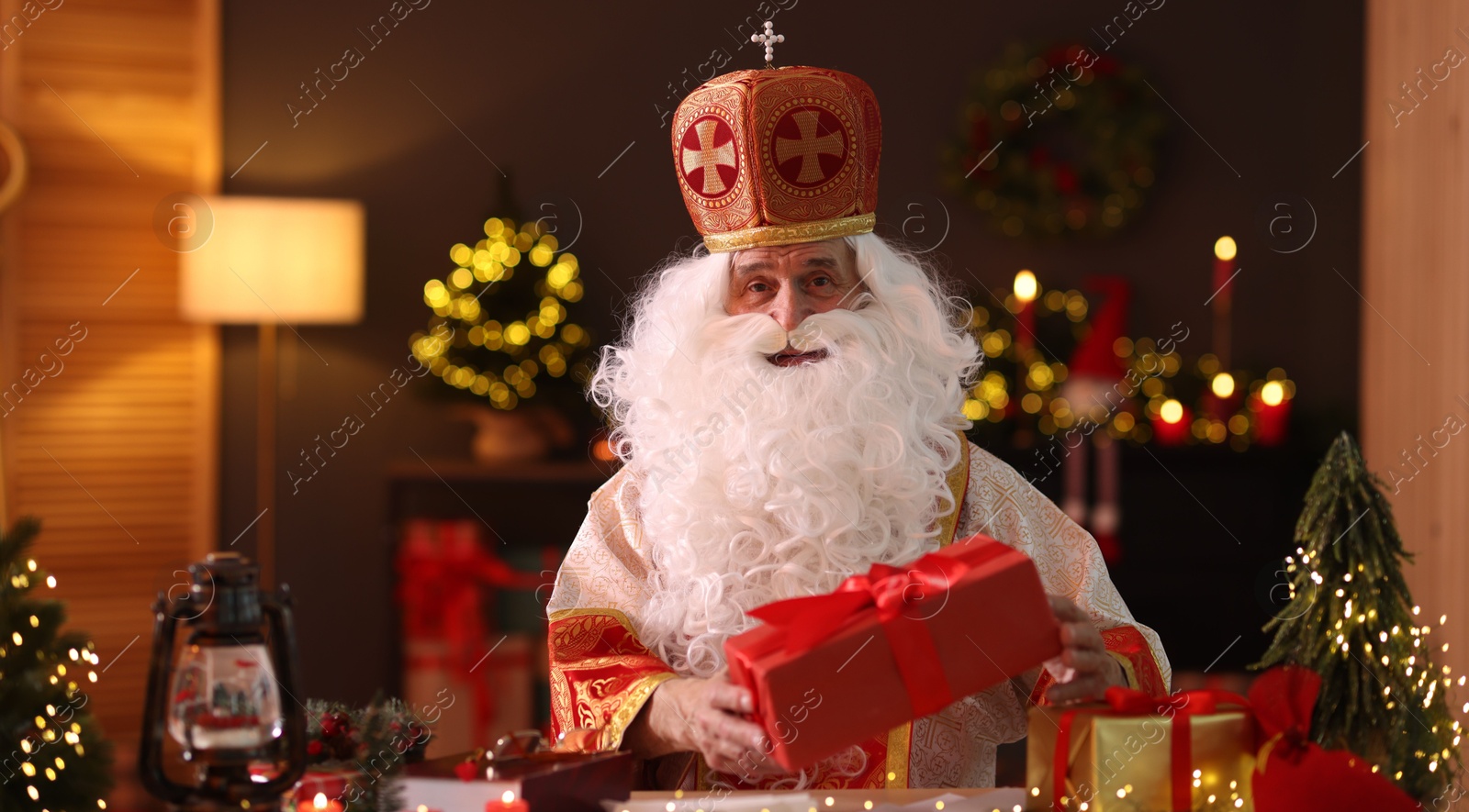 Photo of Saint Nicholas with gifts at desk in room decorated for Christmas