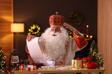 Saint Nicholas with gift list at desk in room decorated for Christmas