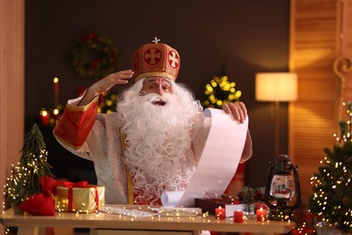 Saint Nicholas with gift list at desk in room decorated for Christmas