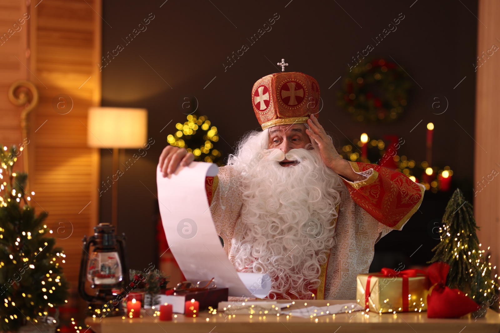 Photo of Saint Nicholas with gift list at desk in room decorated for Christmas