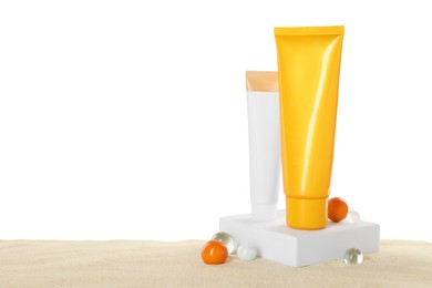 Tubes of sun protection product and decorative stones on sand against white background