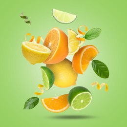 Lime, lemon, orange, zest and leaves in air on light green background