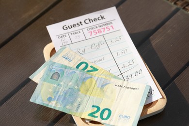 Photo of Wooden plate with payment for order and receipt on table, closeup. Leave tip