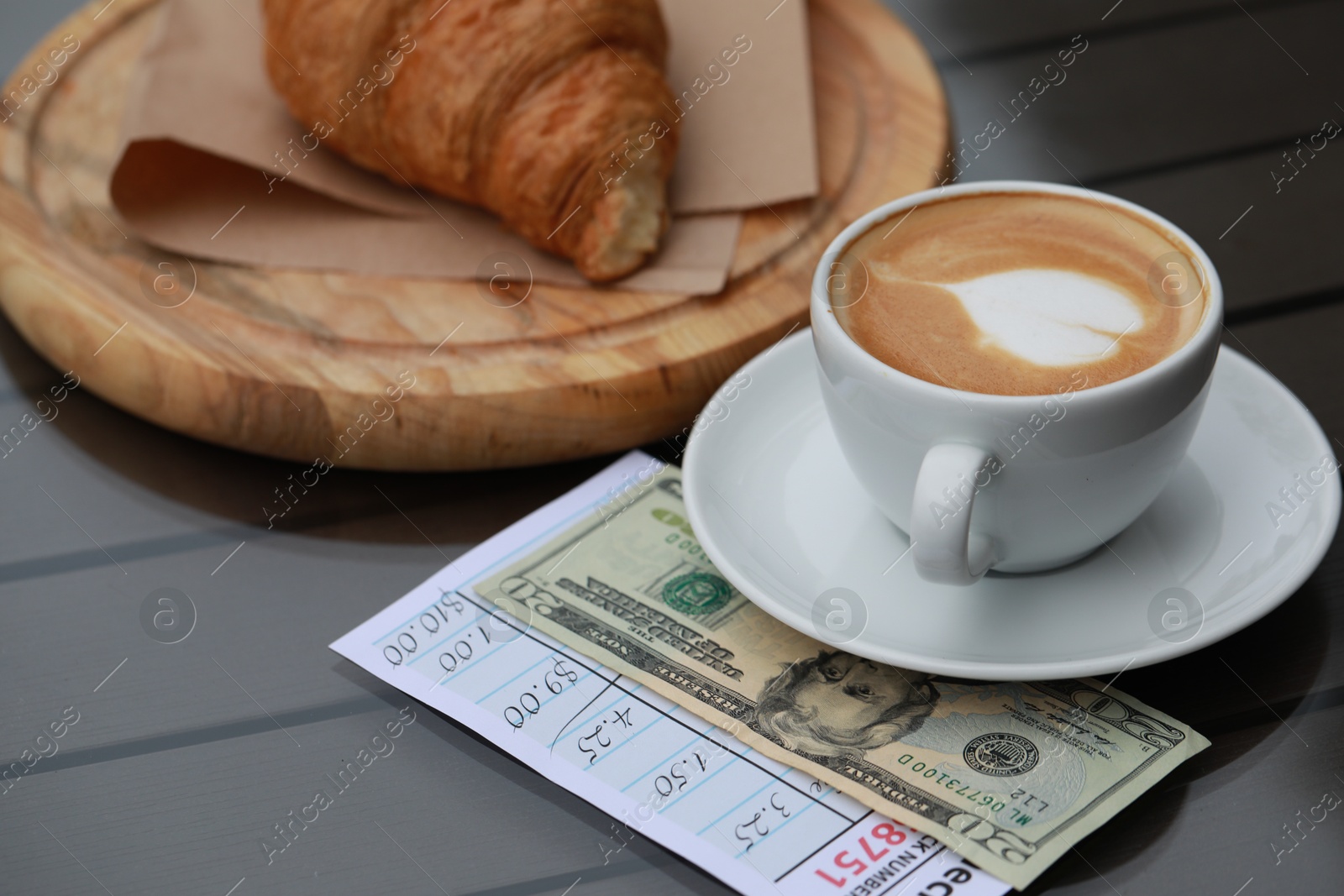 Photo of Croissant, coffee, tip and receipt on wooden table, closeup