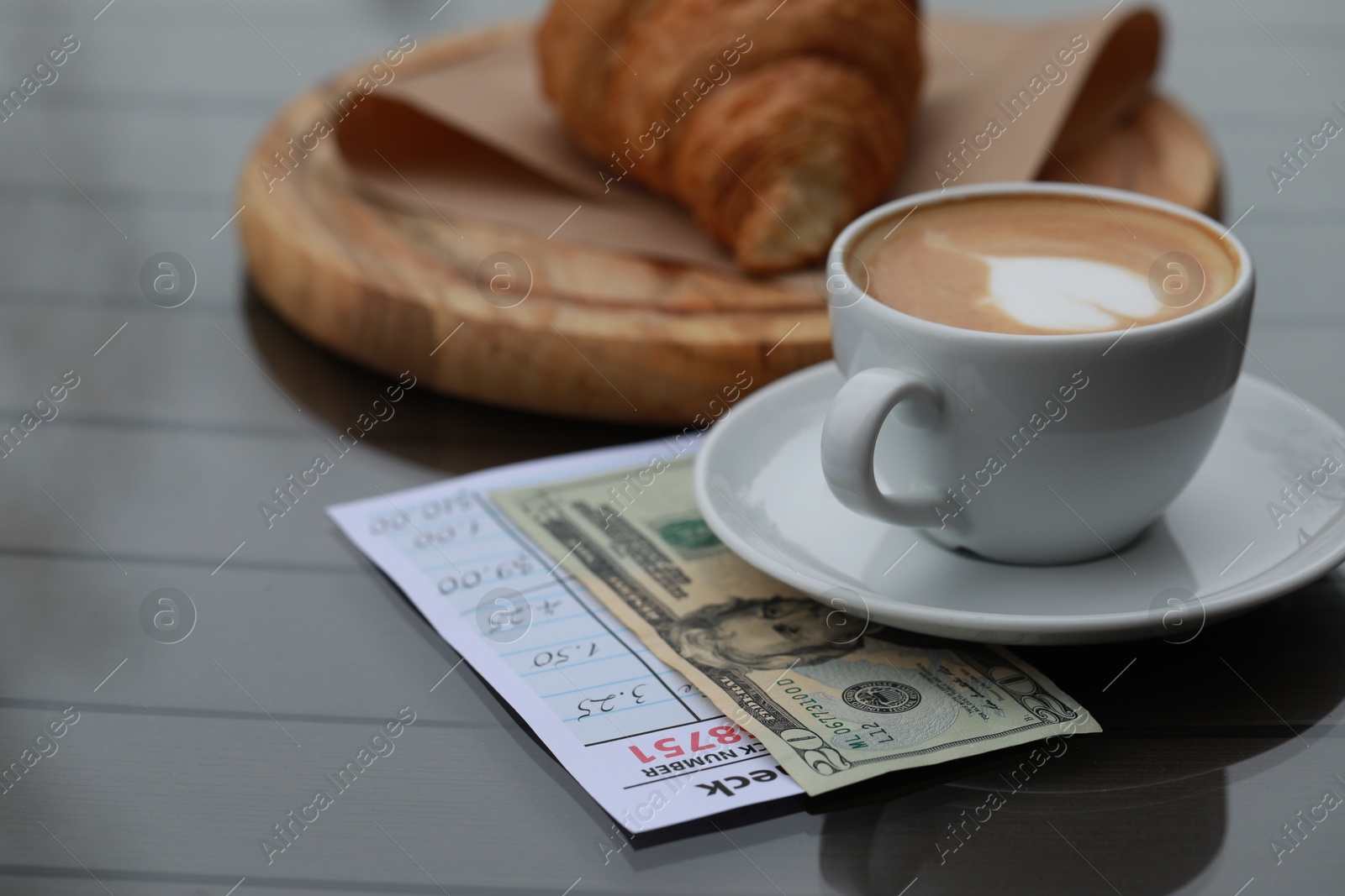 Photo of Croissant, coffee, tip and receipt on wooden table