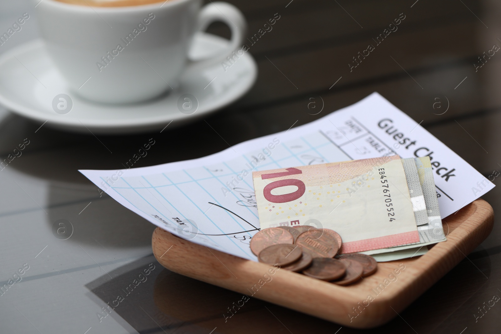 Photo of Tip, receipt and cup of coffee on wooden table, closeup