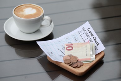 Photo of Tip, receipt and cup of coffee on wooden table, closeup