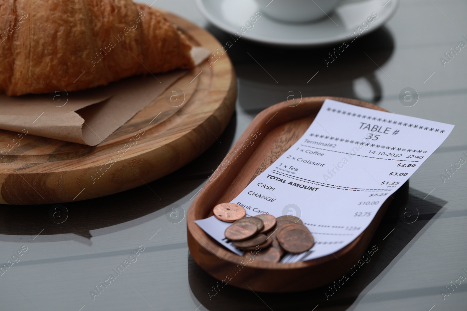 Photo of Tip and receipt near croissant on wooden table, closeup