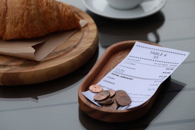 Photo of Tip and receipt near croissant on wooden table, closeup