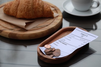 Photo of Tip and receipt near croissant on wooden table, closeup