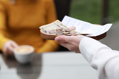 Photo of Waitress holding tips, receipt and payment for order in outdoor cafe, closeup