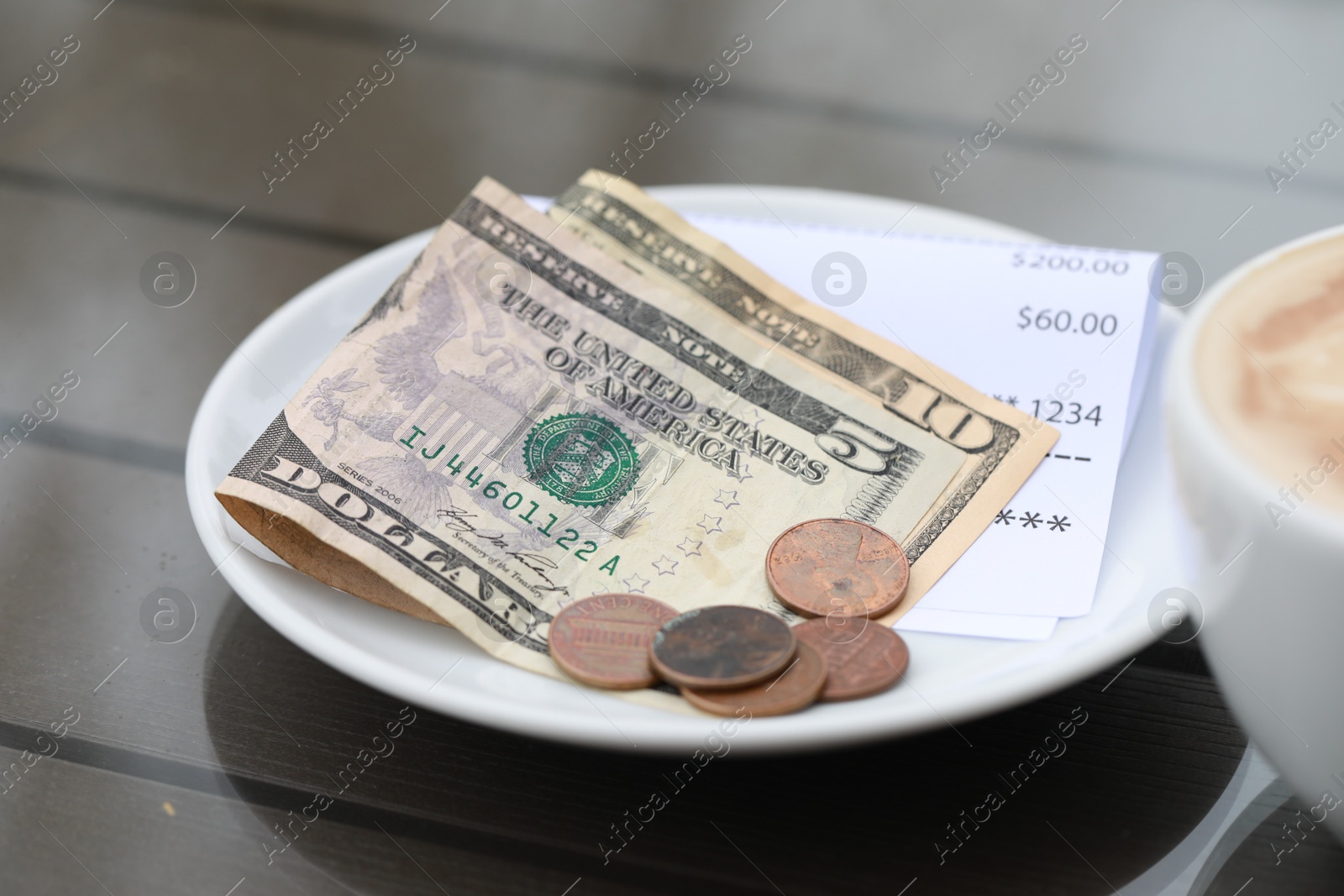 Photo of Tip and receipt on wooden table in cafeteria, closeup