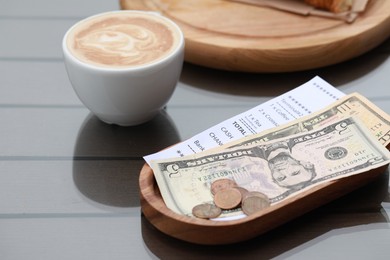 Photo of Tip, receipt and cup with coffee on wooden table, closeup